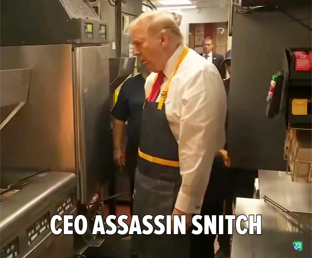 A man with white hair wearing a white shirt, red tie, and a dark apron with yellow straps stands in a commercial kitchen…
