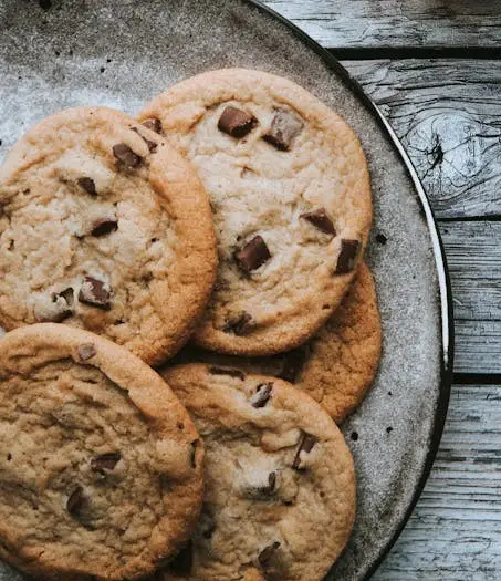 A plate of chocolate chip cookies sits on a rustic wooden surface. The image is overlaid with the text 'i'm not lazy, i'm…