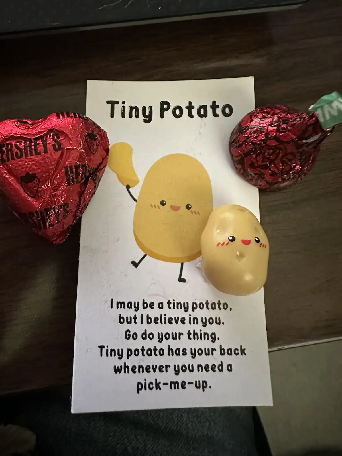 A white card with a cartoon potato and a real small potato on it, surrounded by two red foil-wrapped Hershey's chocolates…