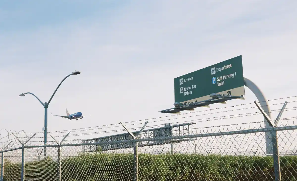 An airport directional sign with arrows for Arrivals, Departures, Rental Car Return, and Self Parking/Valet is visible…