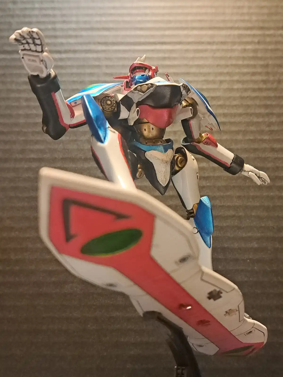 A custom-painted robot model, likely from a Japanese anime or mecha series, is posed dynamically with one arm raised. The…