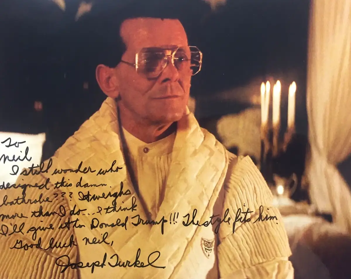 A signed photo of actor Joseph Turkel in a heavy, textured, cream-colored bathrobe and large glasses, looking off to the…