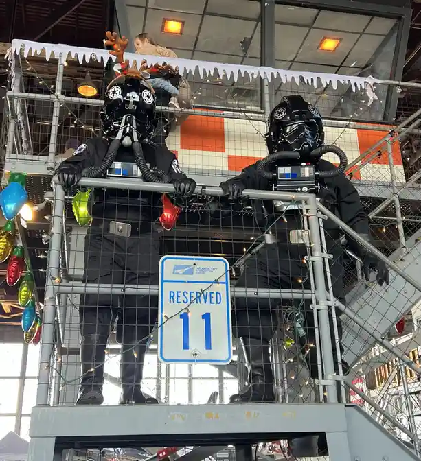 Two people dressed as Star Wars stormtroopers stand on a metal platform decorated with Christmas lights and fake icicles…