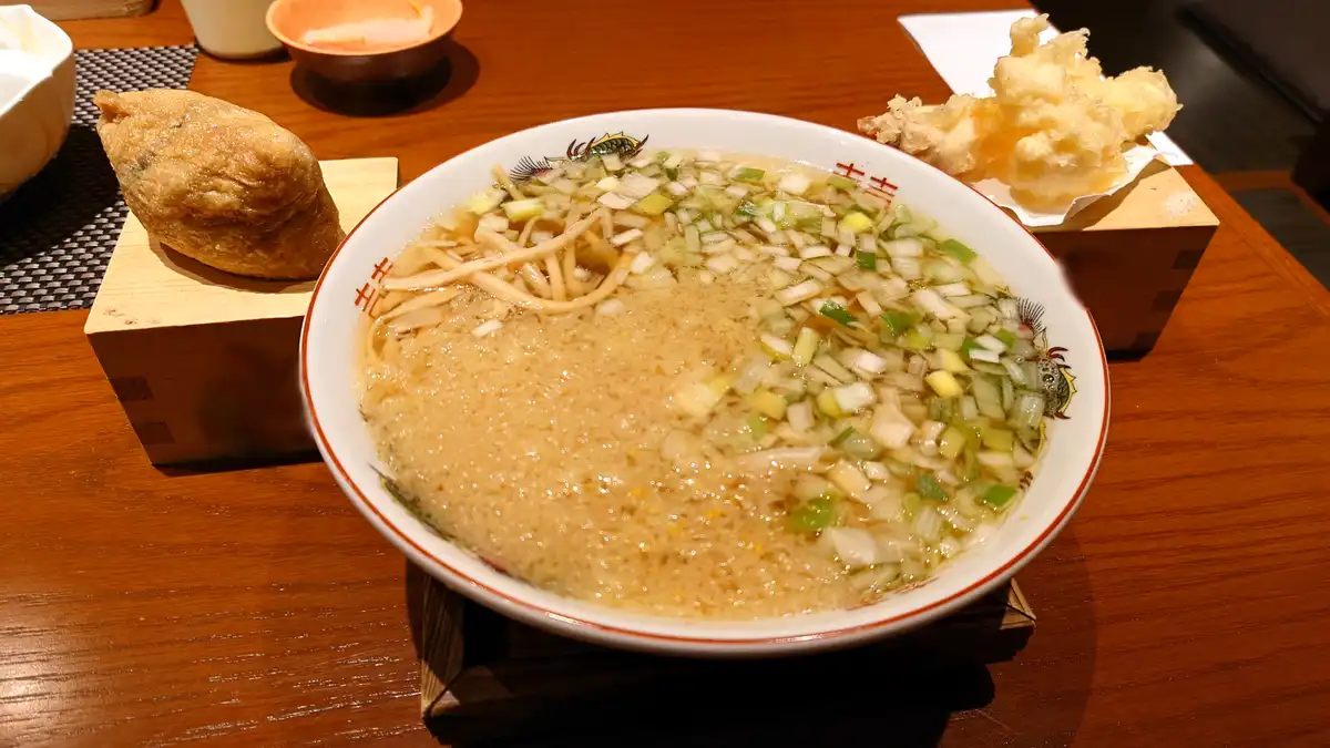 a close-up photo of a bowl of ramen soup with chopped green onions and bean sprouts on top, served on a wooden table with…