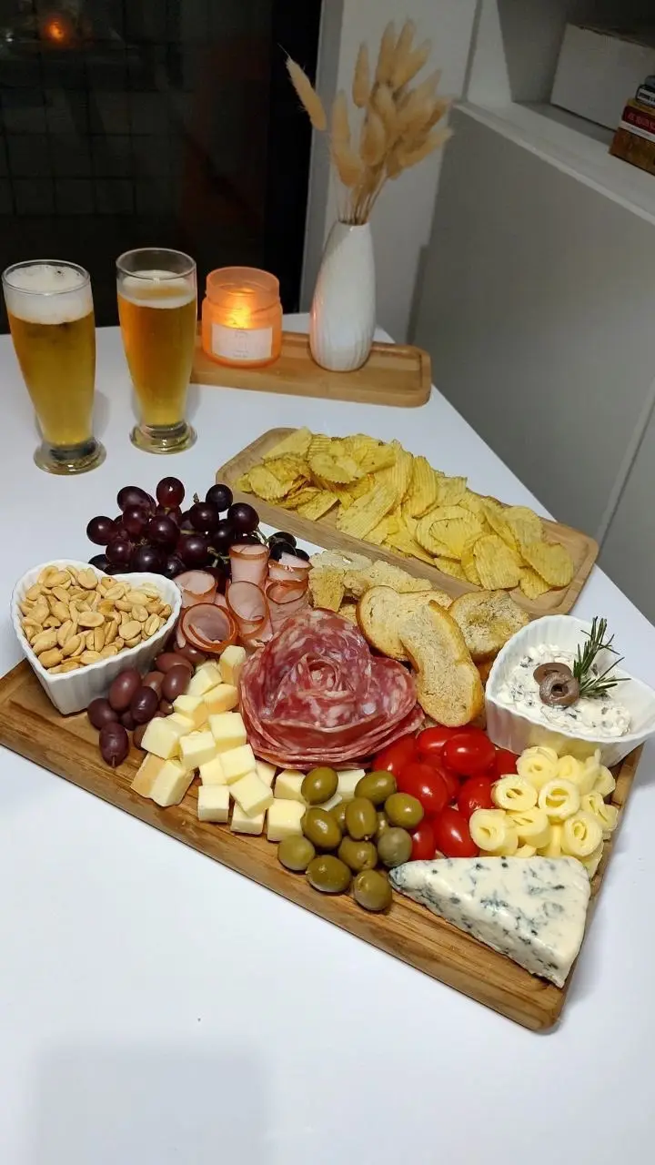 a beautifully arranged charcuterie board with assorted cheeses, meats, grapes, olives, cherry tomatoes, crackers, and chips…