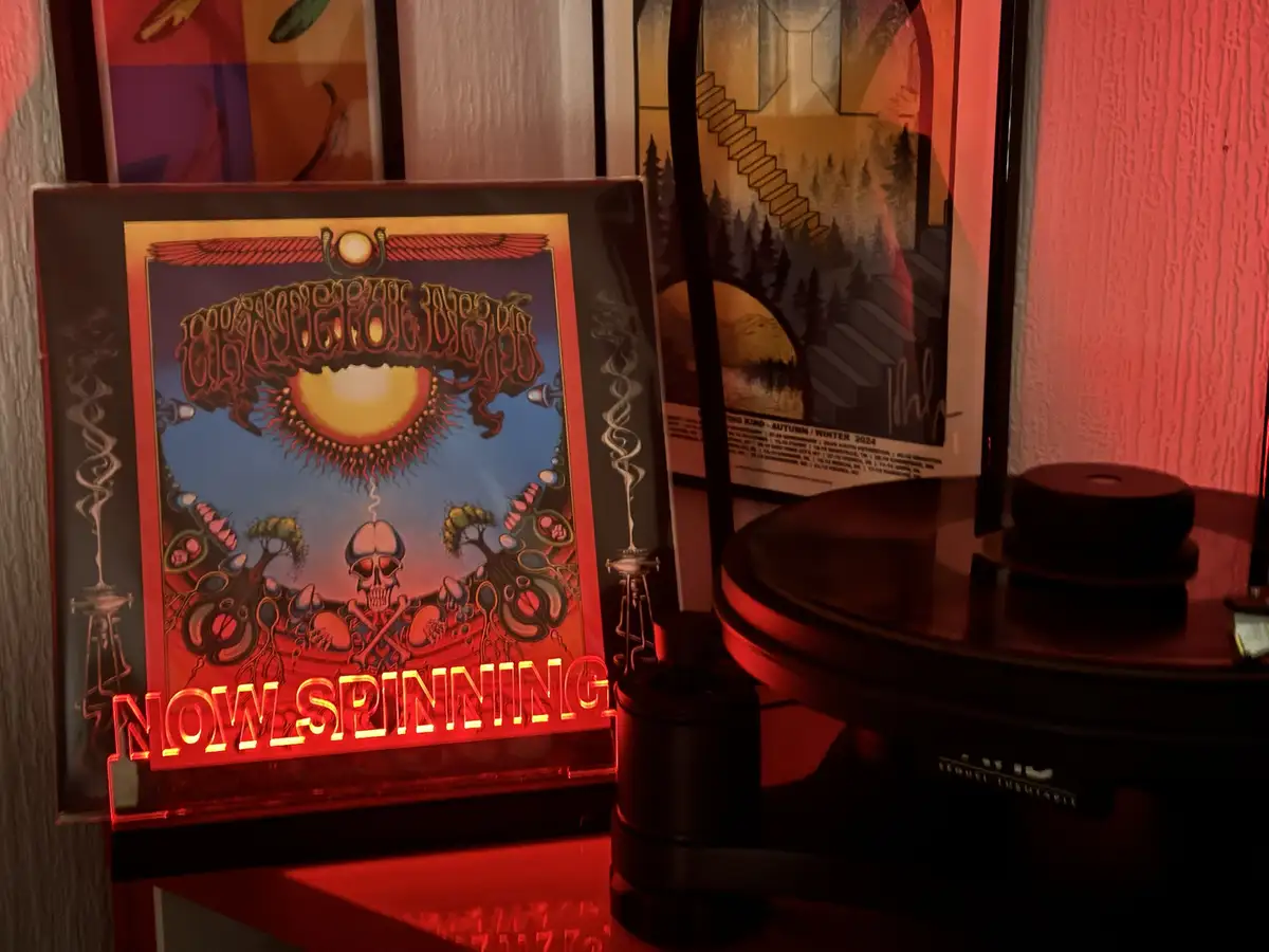 A framed, psychedelic album cover of 'The Grateful Dead' is displayed next to a record player, with a glowing red neon sign…
