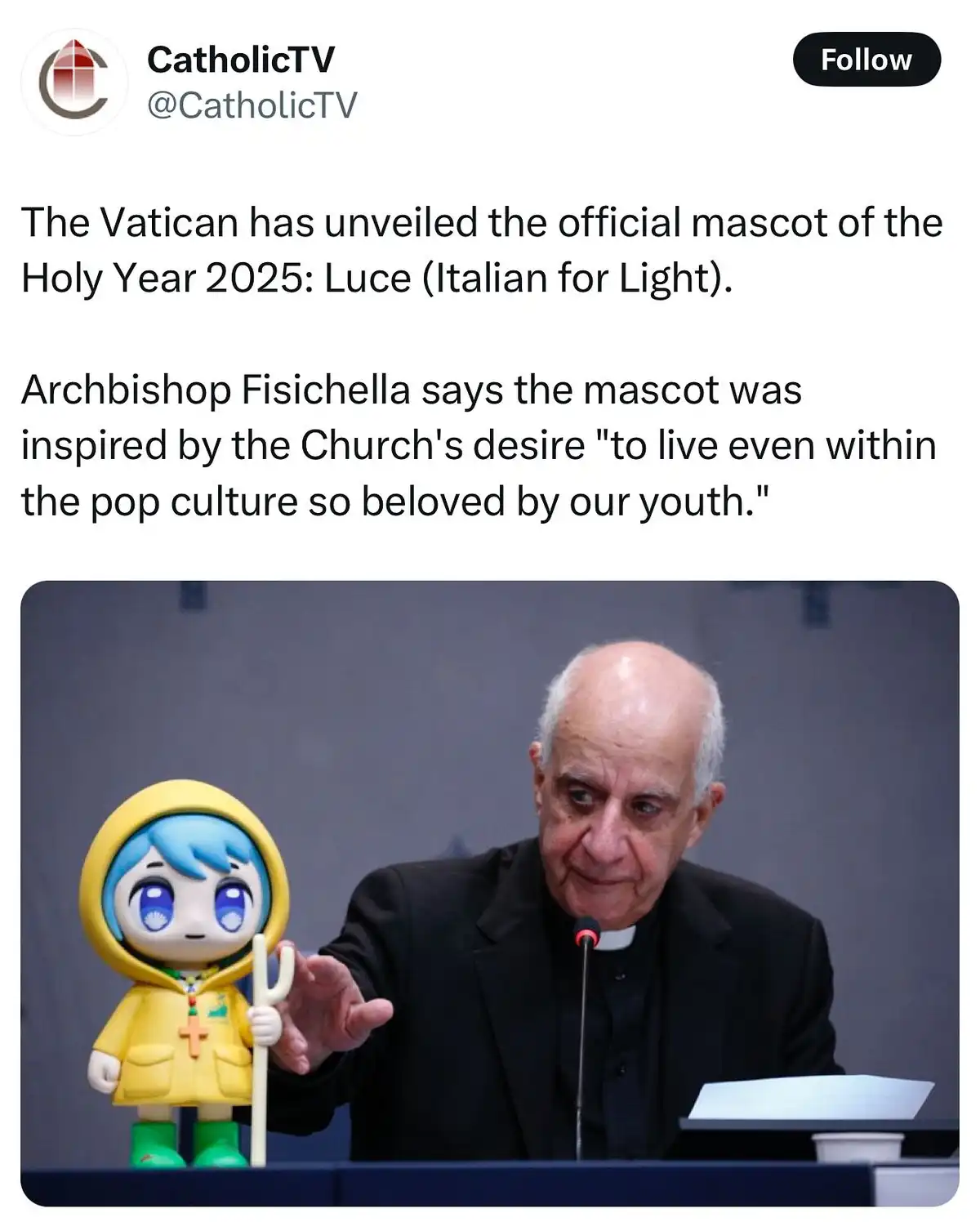 An older man in clerical clothing, identified as Archbishop Fisichella, is seated at a podium holding a small, cartoonish…