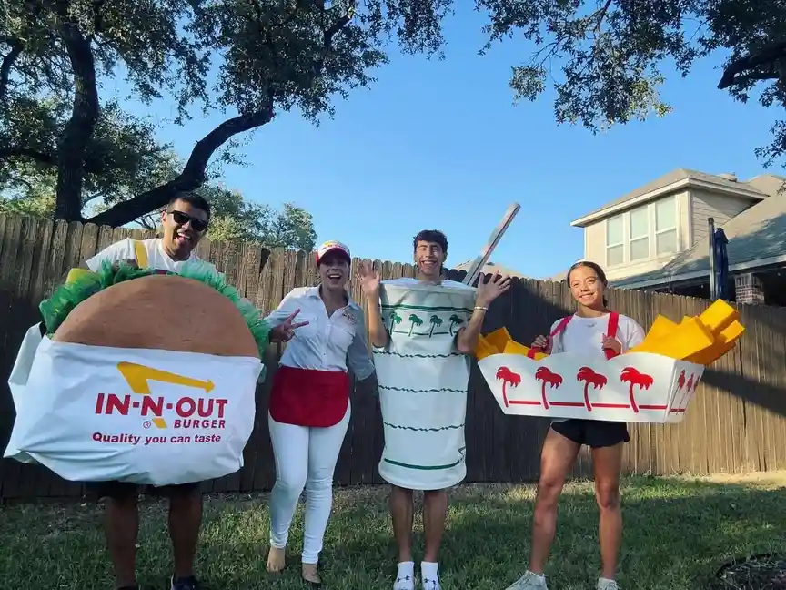 Four people pose outdoors in a backyard, dressed as In-N-Out Burger items: one as a burger with the brand's logo, one as a…