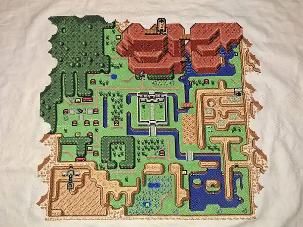 A cross-stitch embroidery on a white fabric depicts the pixelated map from the classic Pokémon Red and Blue video games…
