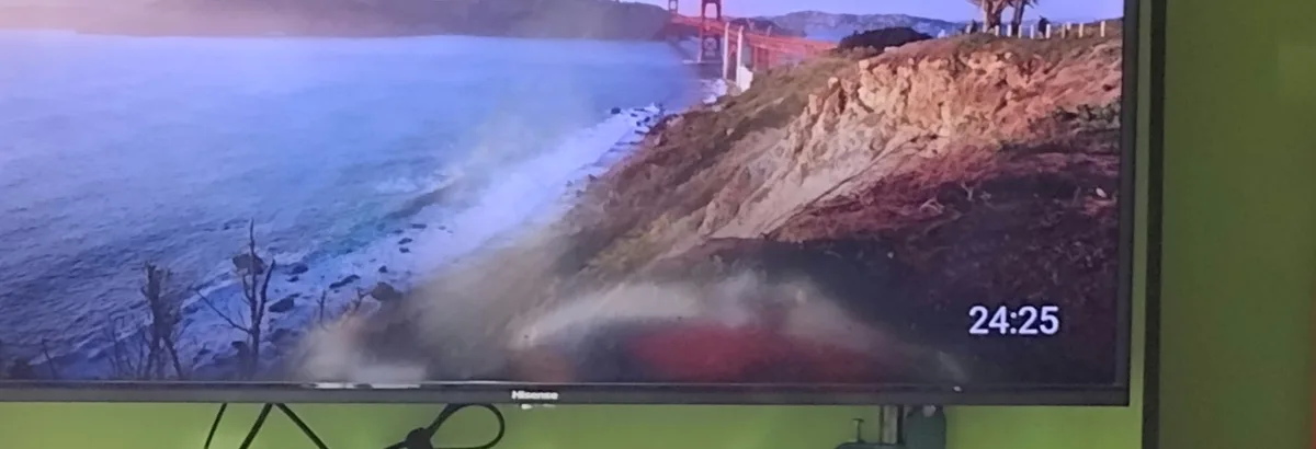 A television screen displays a scenic view of the Golden Gate Bridge with ocean waves crashing against cliffs, overlaid with…