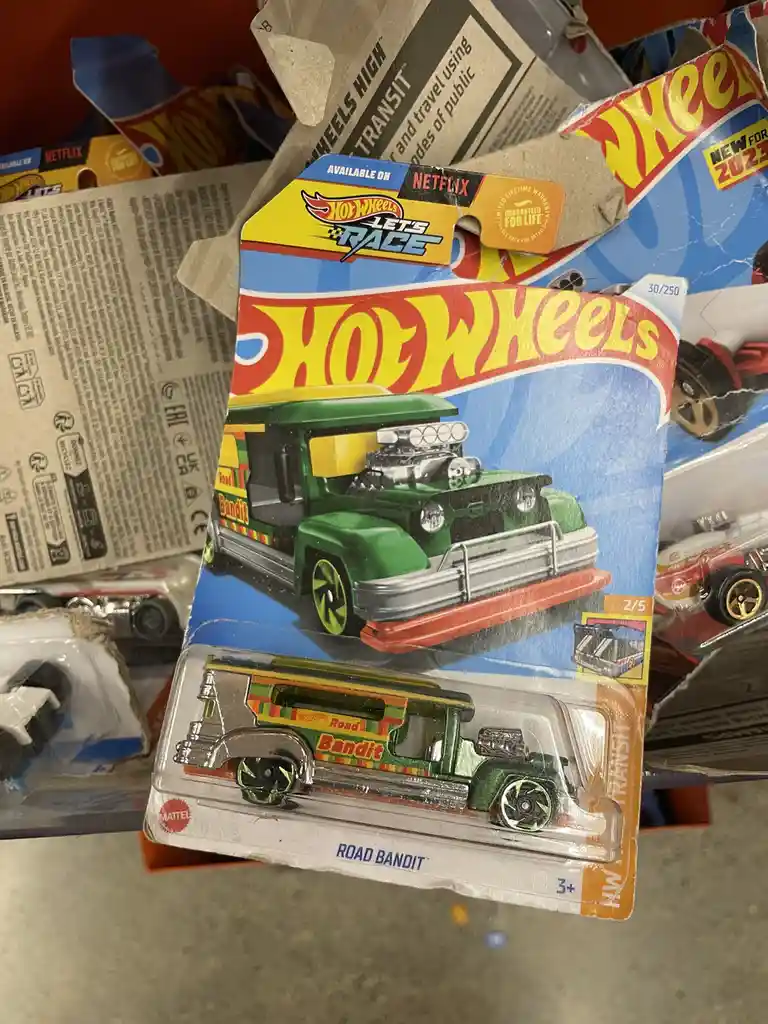 A close-up of a Hot Wheels 'Road Bandit' toy car in its blister pack, which has a sticker that says 'AVAILABLE ON NETFLIX'…