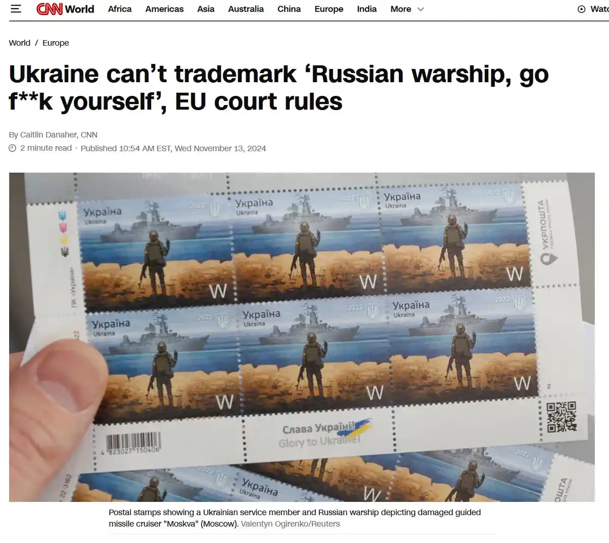 A hand holds a sheet of Ukrainian 2022 postage stamps, each depicting a soldier on a beach pointing at a damaged Russian…