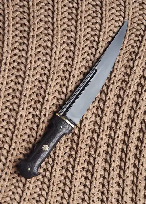 A close-up photo shows a fixed-blade knife with a dark wooden handle and brass accents resting diagonally on a thick…