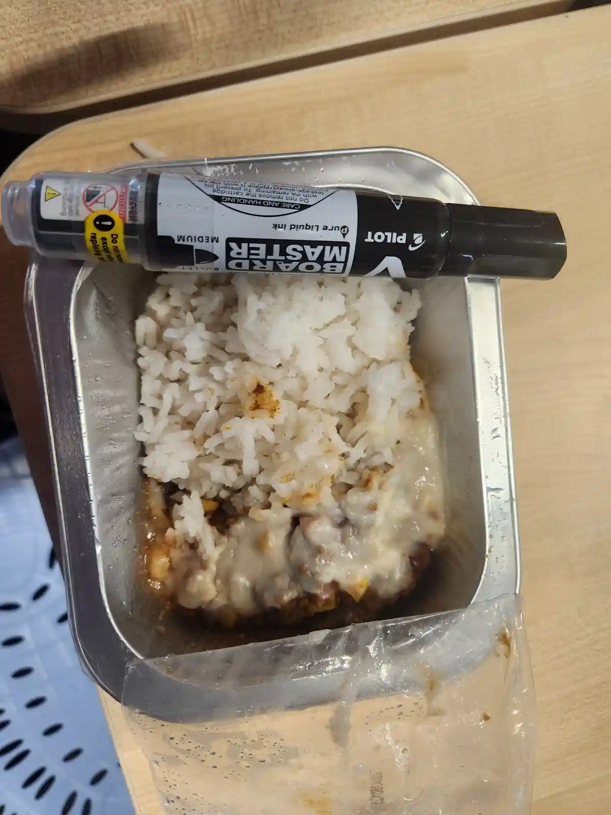 A metal food tray contains a meal of rice and a cheesy dish, with a black Pilot Master Board Bullet marker placed…