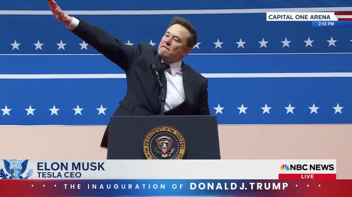 A man in a dark suit stands at a podium with the Seal of the President of the United States, raising his right arm in a…