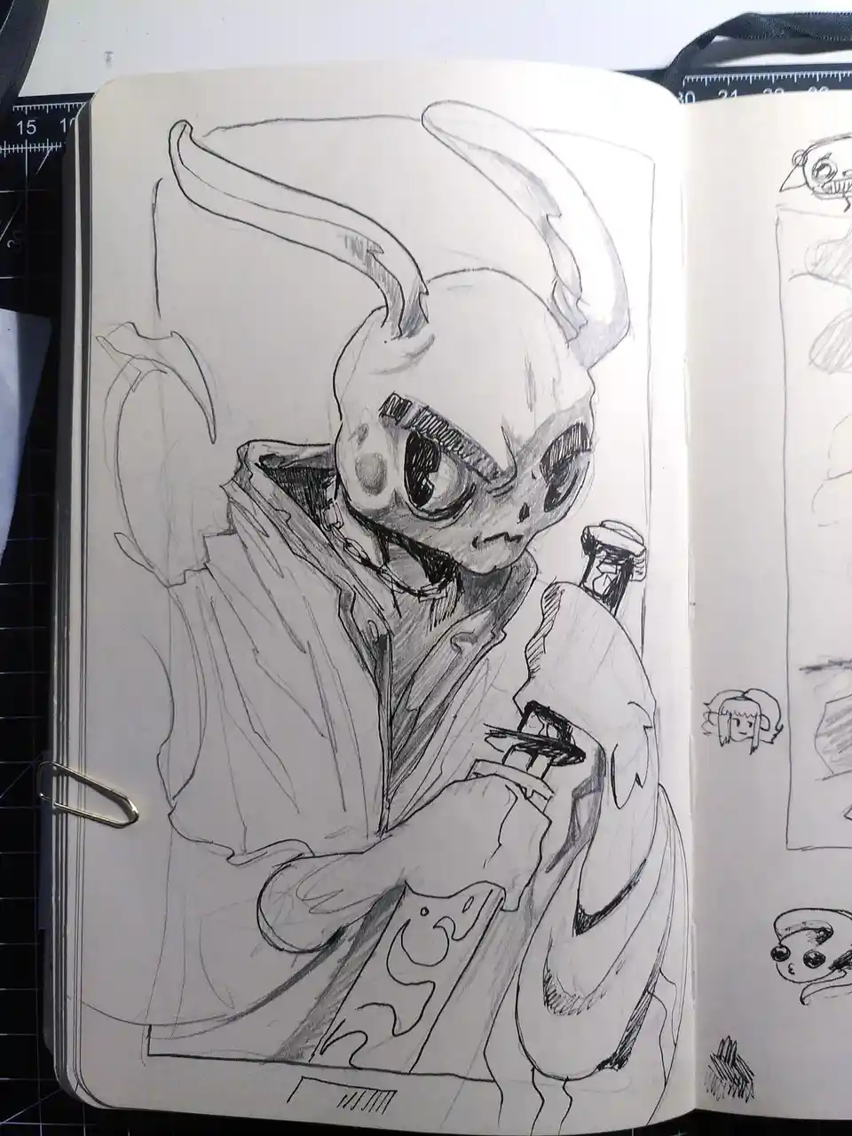 A pencil sketch in an open sketchbook shows a cartoonish, horned creature with large eyes, wearing a coat and holding a…