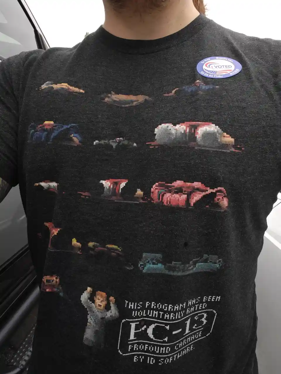 A person wears a dark gray t-shirt featuring pixelated graphics of various cars and a character, with text at the bottom…