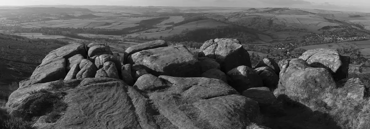 A black-and-white panoramic photo shows a vast, rolling countryside with fields, forests, and distant villages, viewed from…
