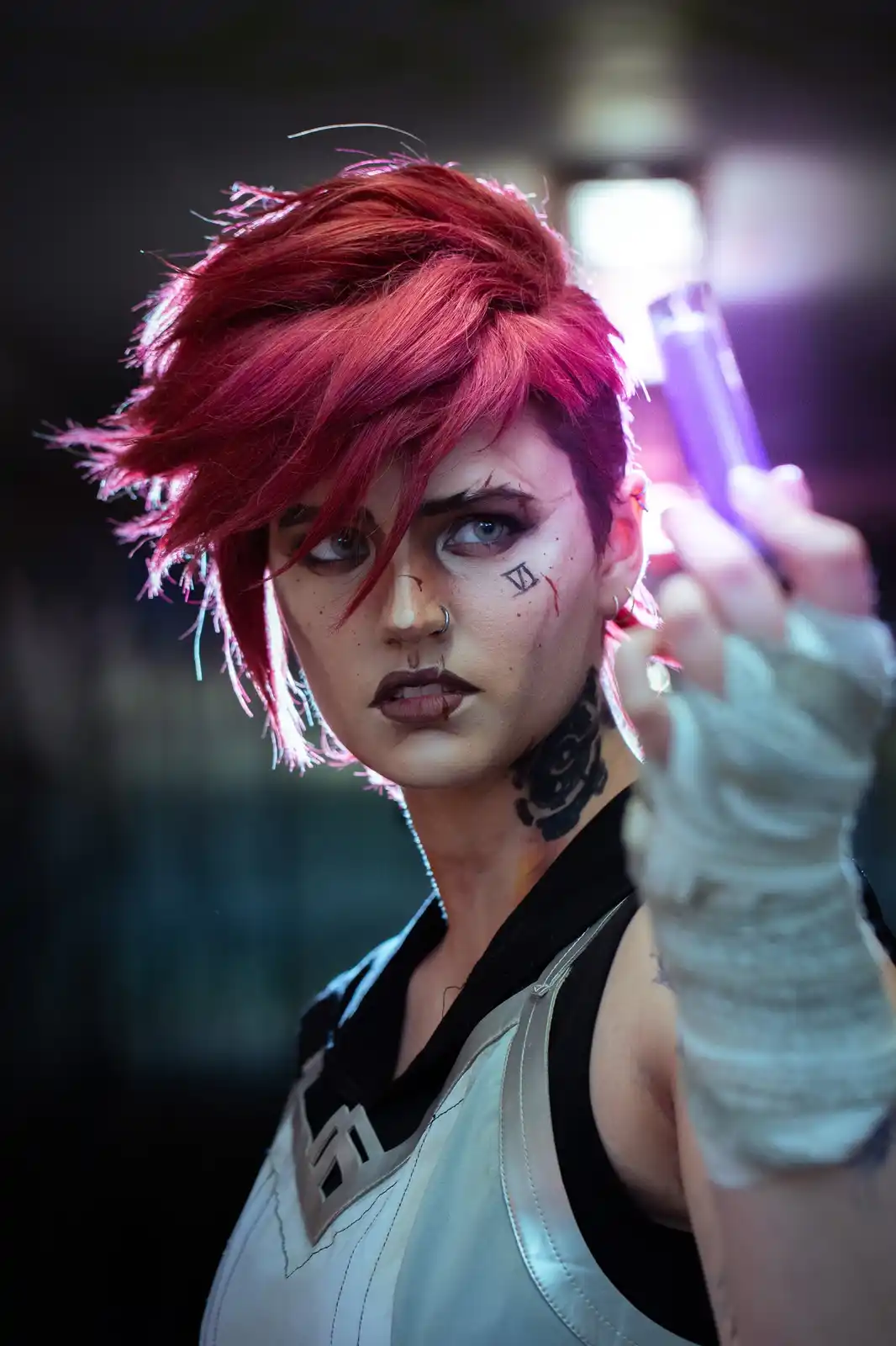 A person with short, spiky red hair and intense blue eyes, wearing a white and black outfit with a visible tattoo on their…