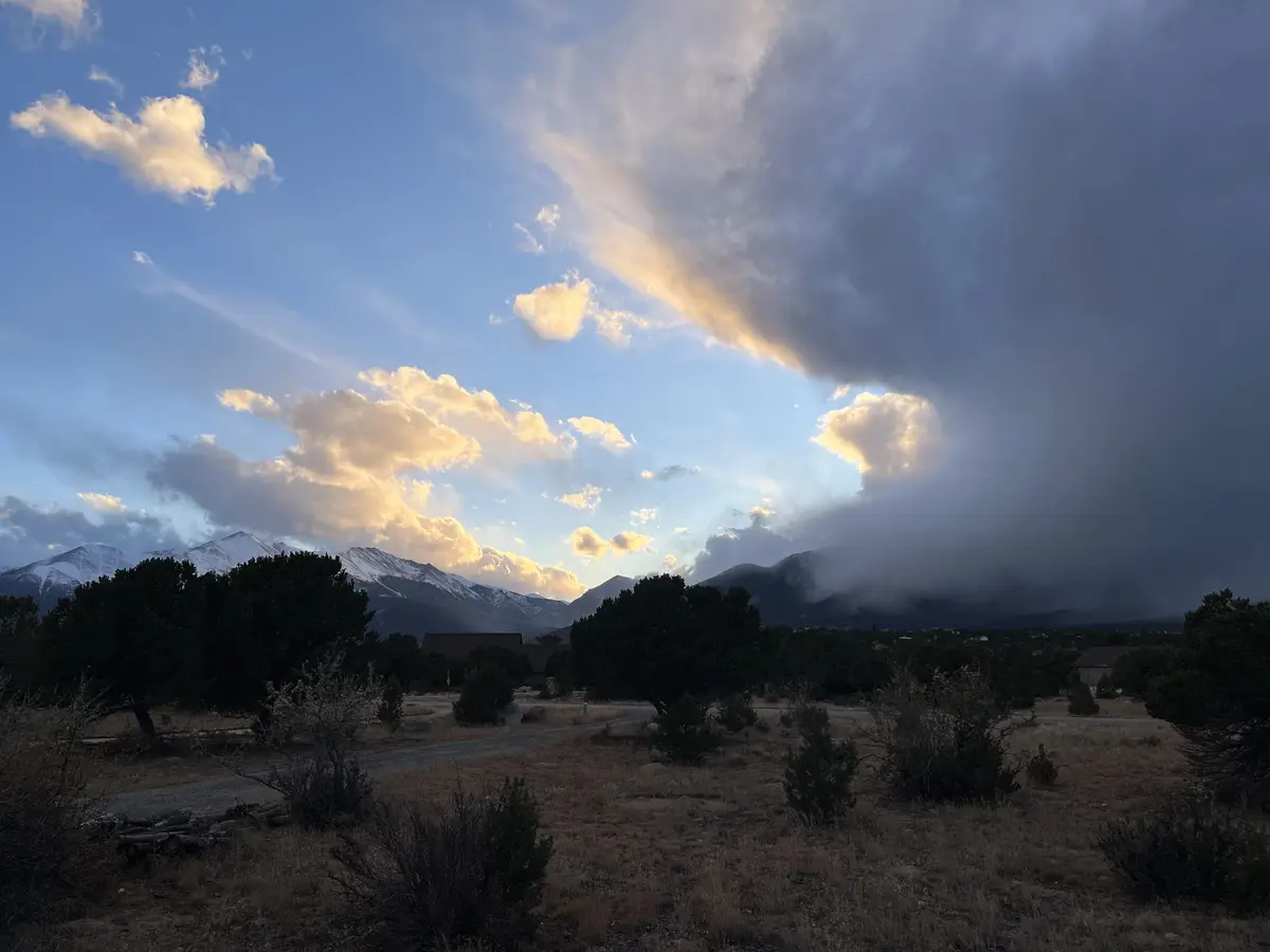 A scenic landscape photo shows a dramatic sky with golden clouds illuminated by sunset or sunrise, contrasting with dark…