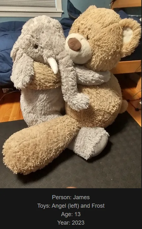 Two large stuffed animals, a grey elephant named Angel and a tan bear named Frost, are sitting together on a dark mat in a…