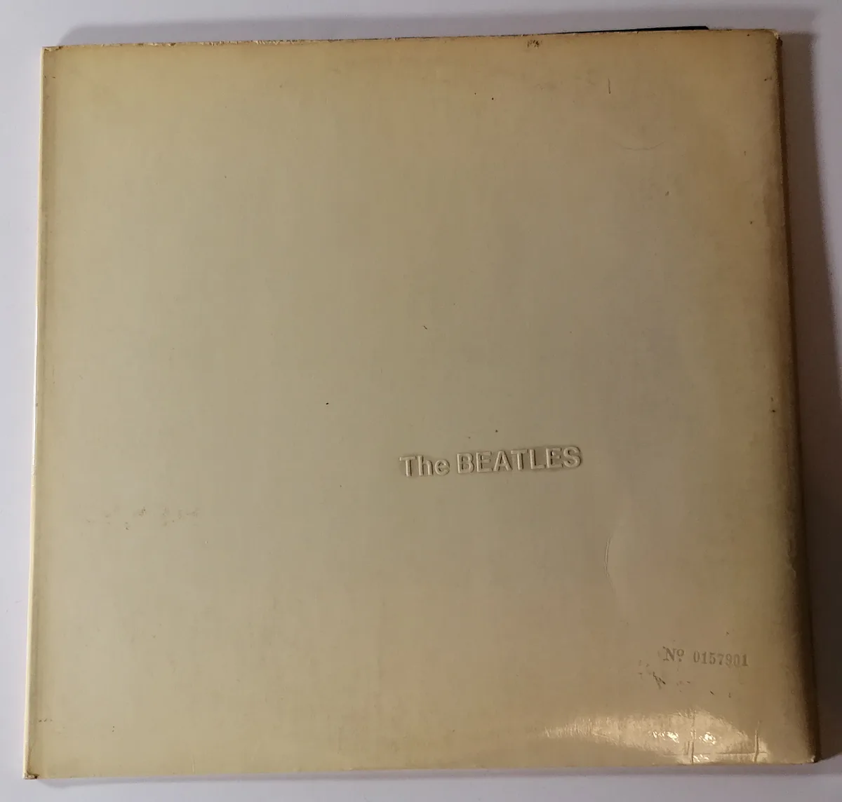 A close-up photo of the plain, off-white back cover of a vinyl record sleeve for The Beatles, showing the embossed band name…