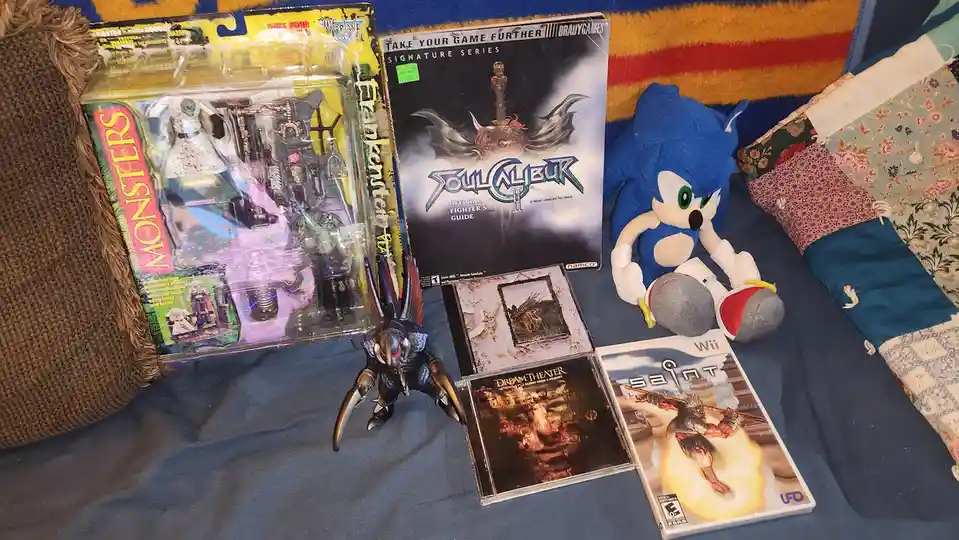 A collection of vintage video game merchandise and media is laid out on a blue blanket, including a 'Monsters' action figure…