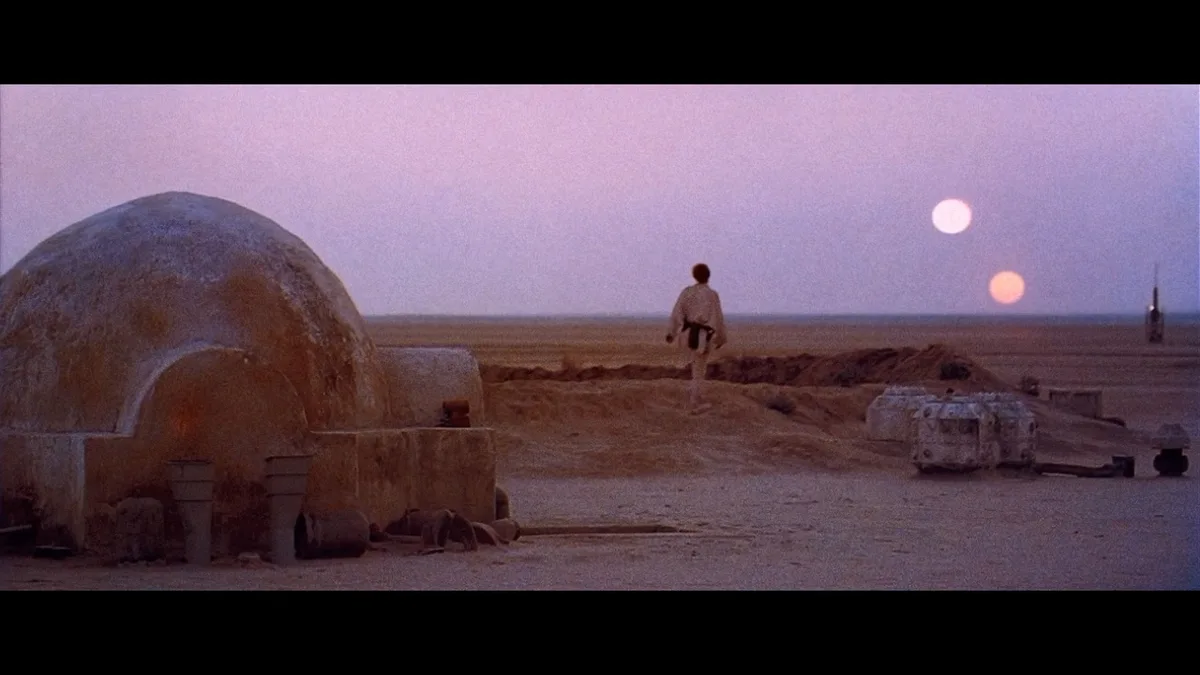 A still from Star Wars: Episode IV - A New Hope shows a young boy in a desert landscape with a dome-shaped building on the…