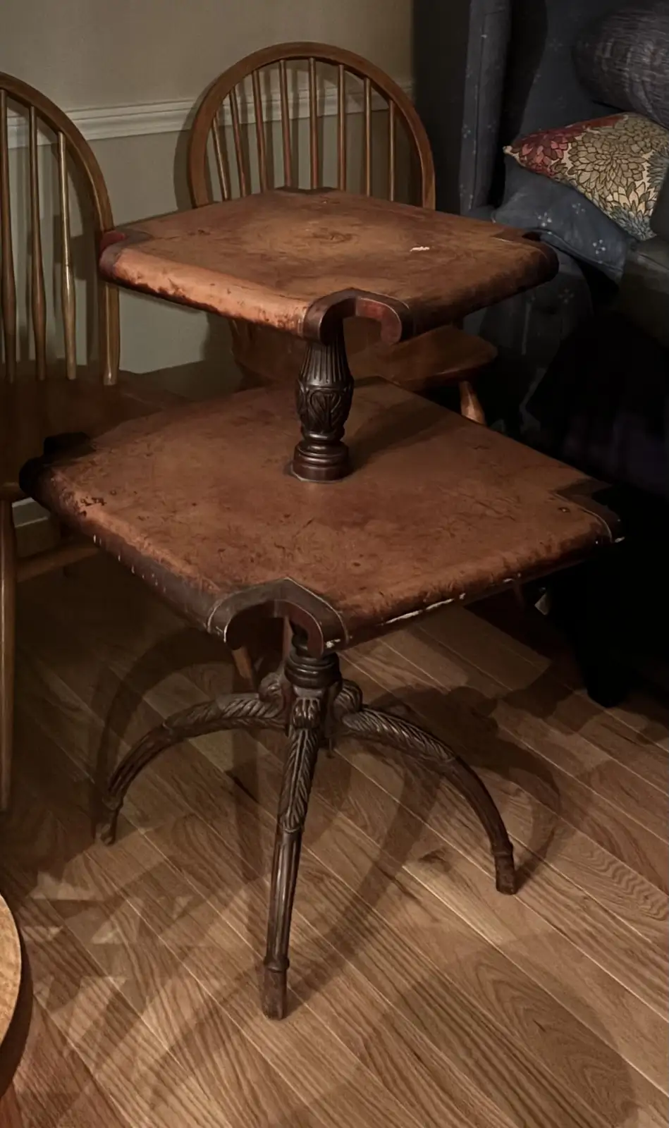 A vintage wooden table with a single ornate central leg and a square top, placed atop another matching wooden chair…