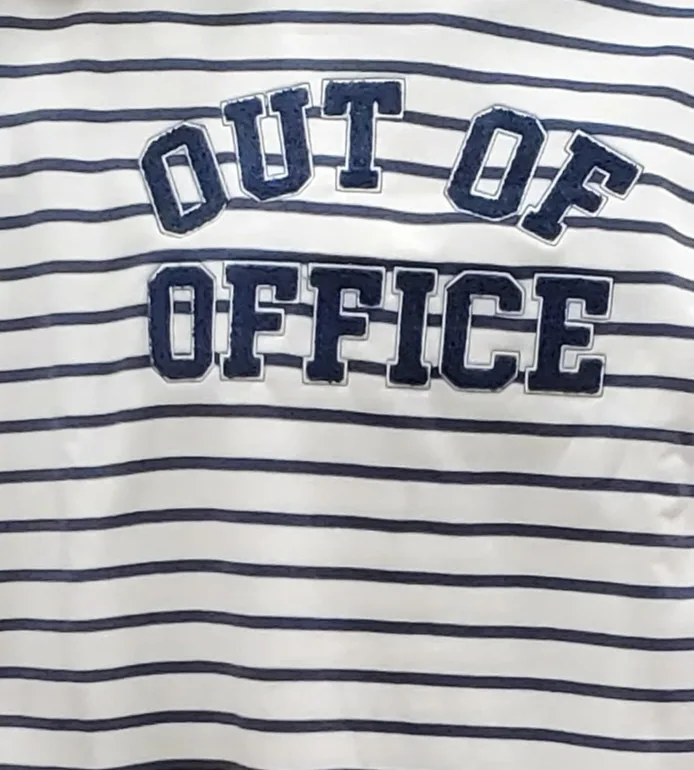 A close-up of a white and navy blue horizontally striped shirt with the words 'OUT OF OFFICE' embroidered in large, bold…