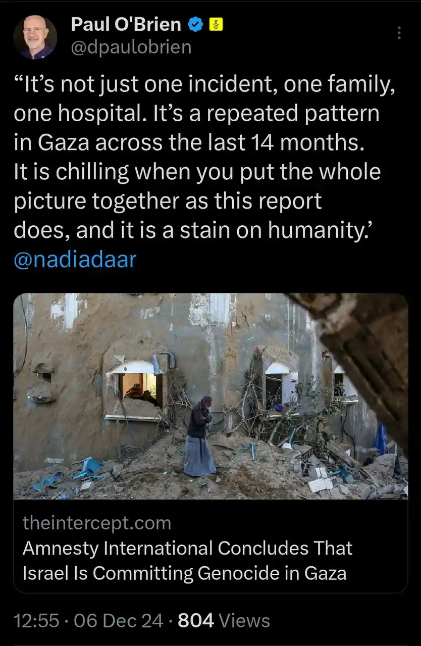 A screenshot of a tweet by Paul O'Brien showing a photo of a person standing amidst rubble in front of a heavily damaged…