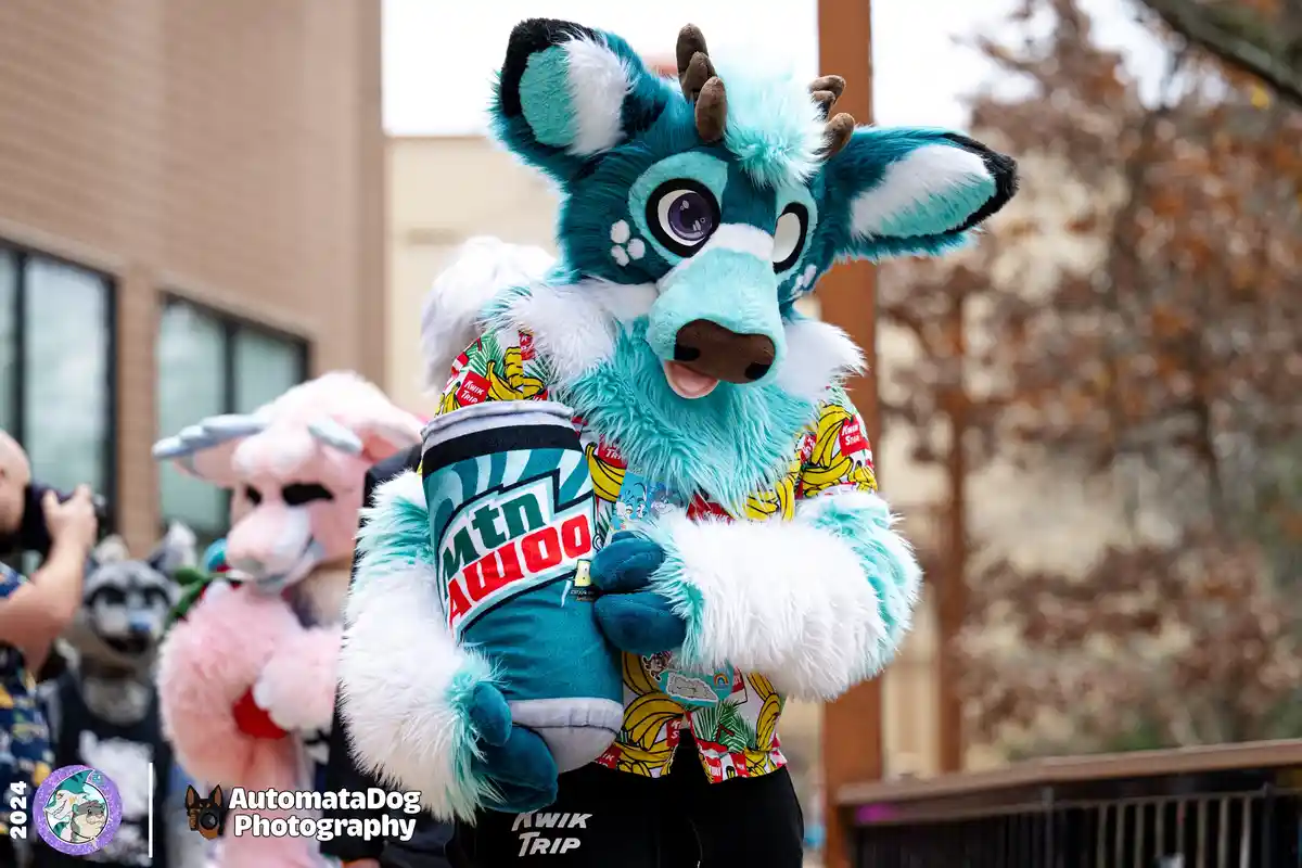 A person in a blue and white furry costume resembling a goat or deer holds a large plush Mountain Dew can that has been…