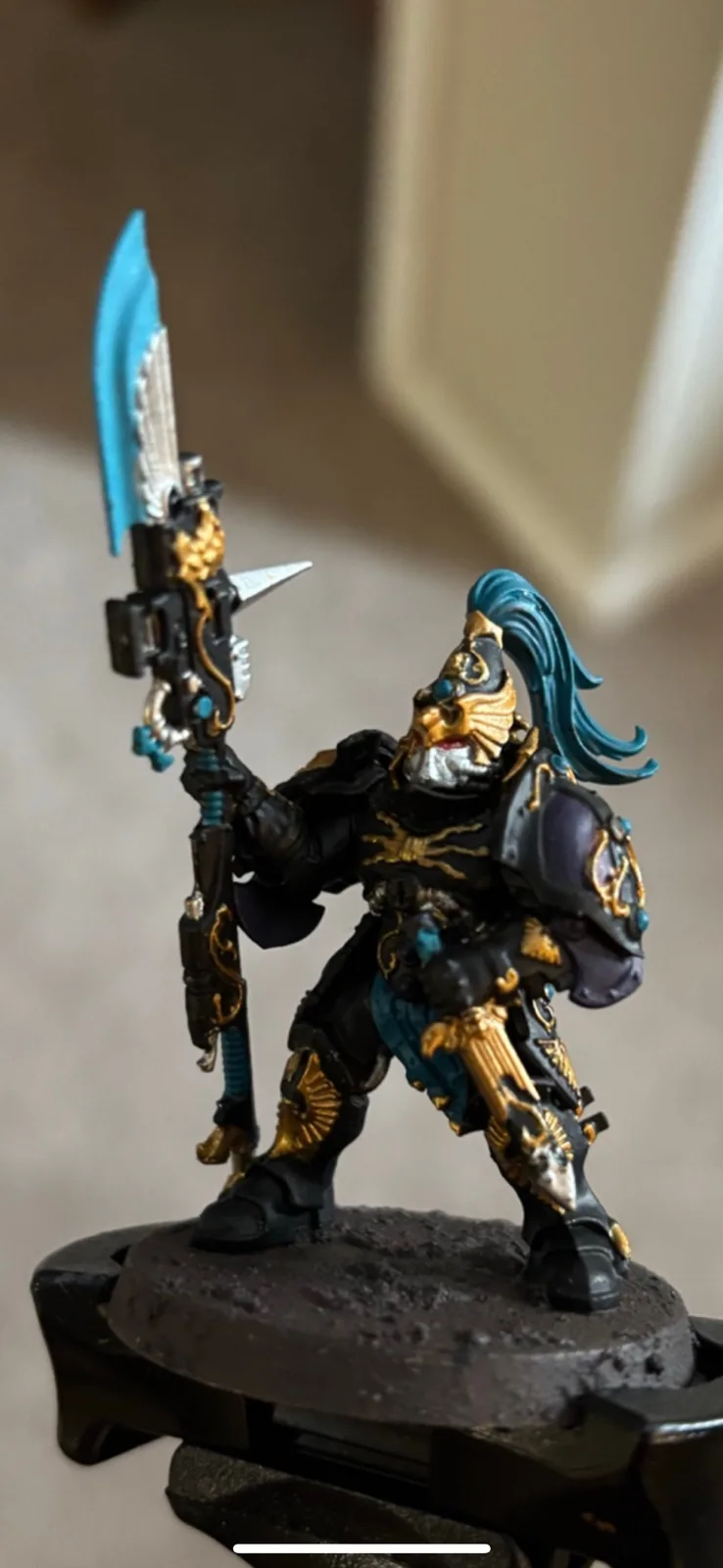 A heavily painted fantasy miniature figure, likely from Warhammer 40,000, stands on a rocky base holding a large ornate…