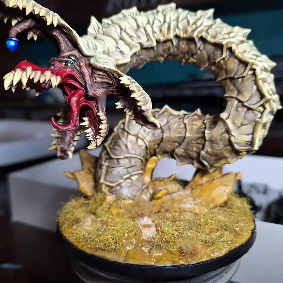 A highly detailed, painted miniature of a coiled, monstrous dragon with a gaping red mouth, sharp teeth, and a blue orb…