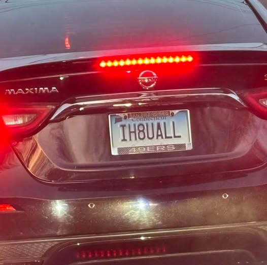 The rear of a black Nissan Maxima with its brake lights on, showing a Connecticut license plate that reads 'IH8UALL' with a…