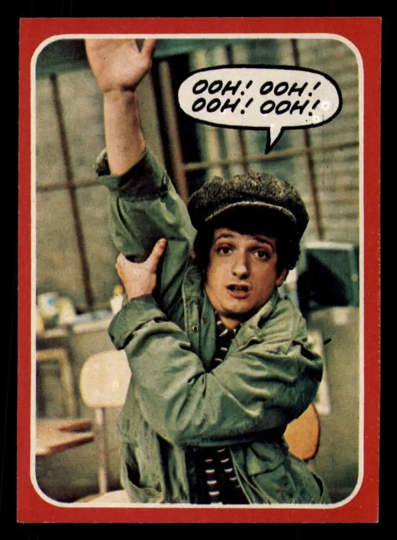 A vintage trading card-style image shows a young man in a green jacket and flat cap, seated and raising his right arm…