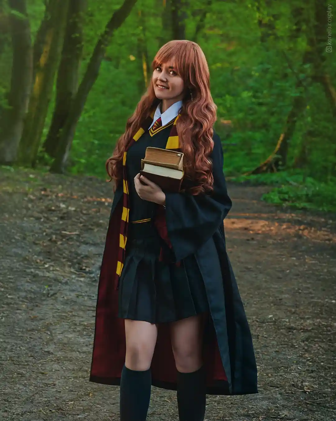a person in a harry potter cosplay as a female character with long red hair, wearing a dark blue robe, a maroon and gold…