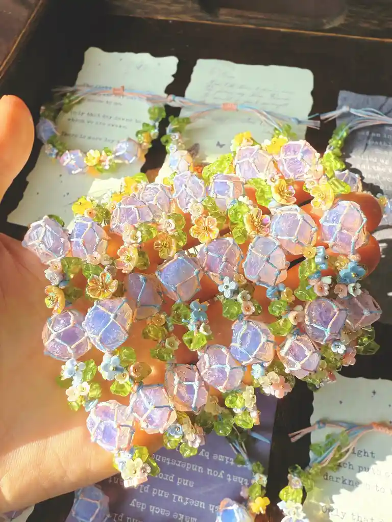 A hand holds a large, intricate macrame bracelet made of purple, green, and yellow beads shaped like flowers and geometric…