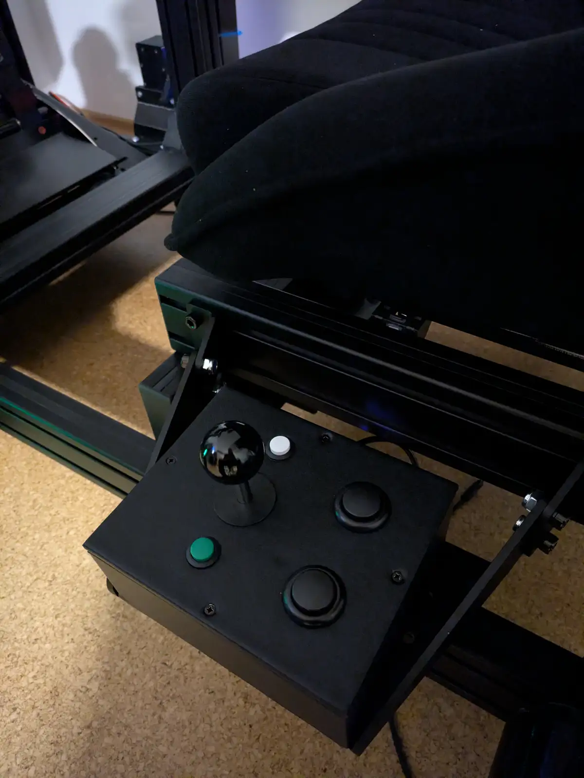A close-up photo shows a black flight simulator joystick controller with a central stick, a green button, and two black…