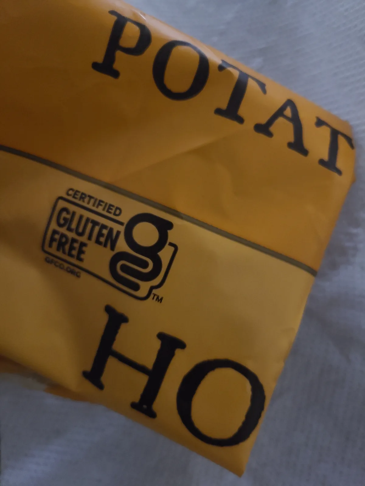 A close-up of a yellow potato chip bag with the word 'POTATO' at the top and 'HO' at the bottom, with a 'Certified Gluten…