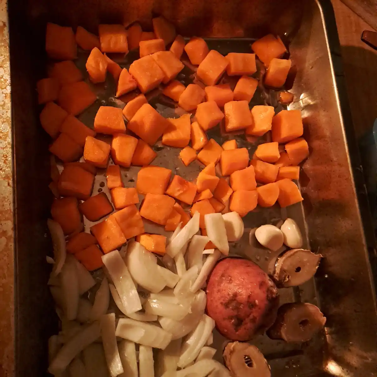 A baking tray contains chopped orange sweet potatoes arranged to resemble a face, with sliced onions forming the eyes…