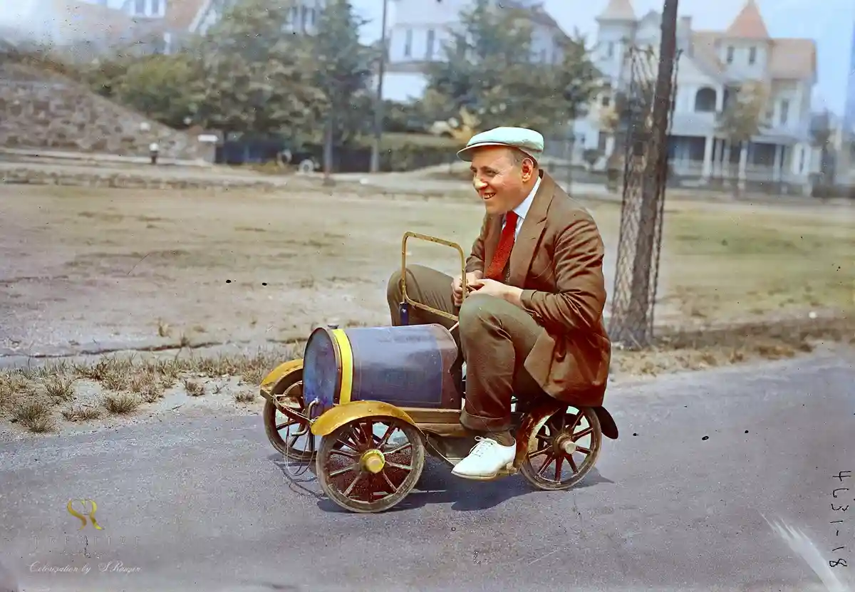 A man riding a child's toy car on the streets of 1920s New York, colorized by Sergey V. Rauzin in 2025