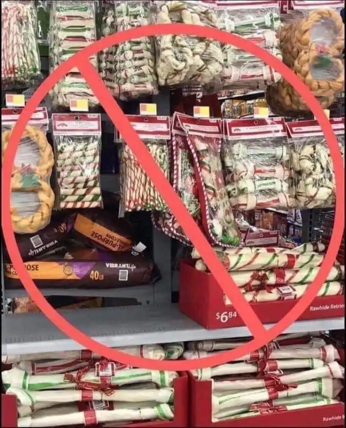 A store shelf filled with holiday-themed dog chew toys, mostly rawhide bones wrapped in red and green striped paper, is…
