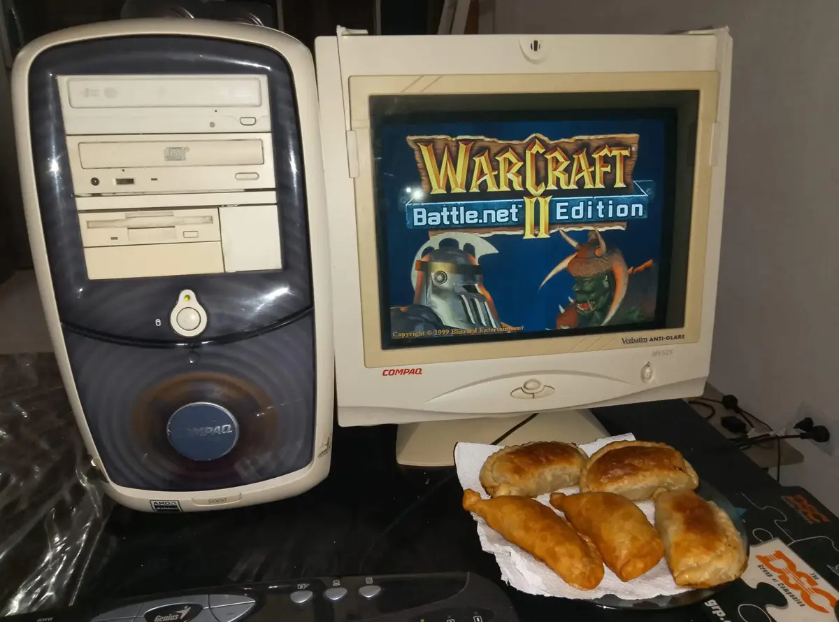 An old beige Compaq desktop computer with a CRT monitor displaying the Warcraft II Battle.net Edition title screen, next to…