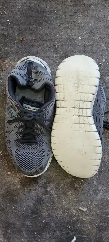 A pair of grey Skechers Skech-Knit sneakers are shown from above, one shoe facing forward with laces tied and the other…