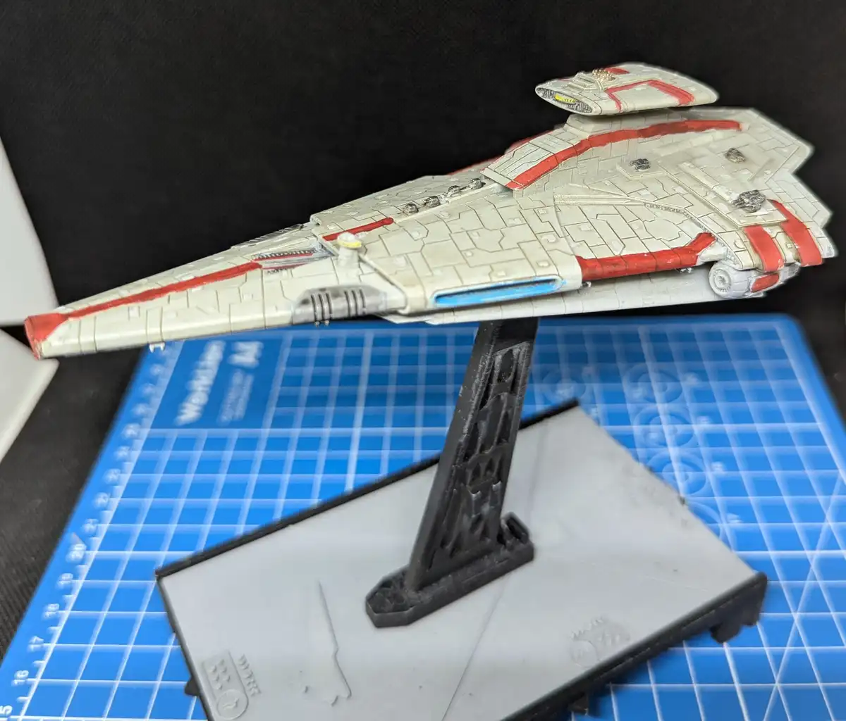 A detailed, hand-painted model of a Star Wars starship, likely a Star Destroyer, is displayed on a black stand atop a blue…
