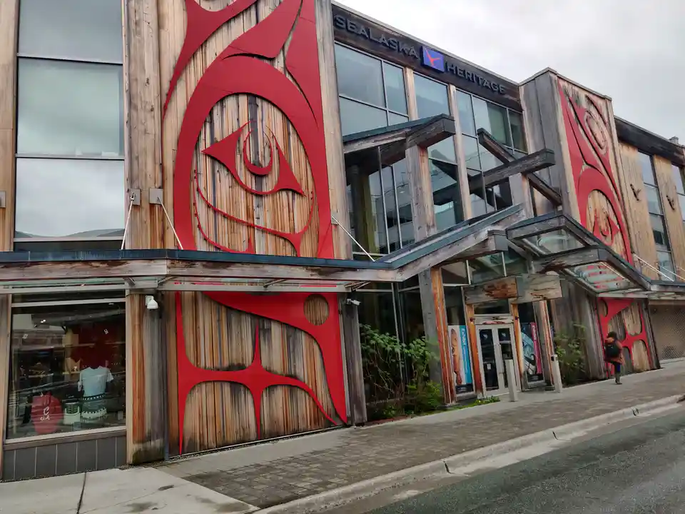 An exterior photo of the Sealaska Heritage building, featuring prominent red indigenous art cutouts on weathered wooden…
