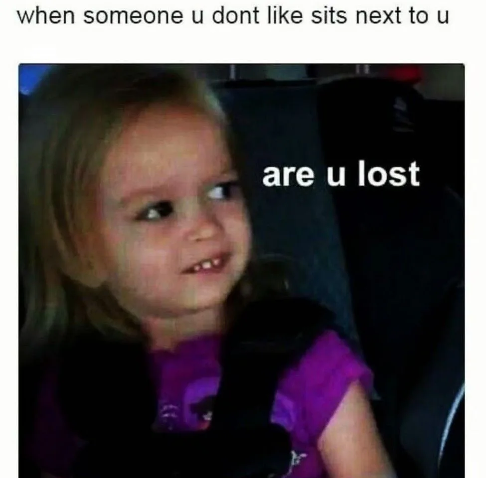 A young girl with blonde hair and a purple shirt sits in a car seat, looking sideways with a skeptical, slightly annoyed…