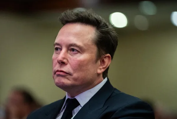 a close-up photo of elon musk looking slightly to his right with a neutral to mildly concerned expression, wearing a dark…