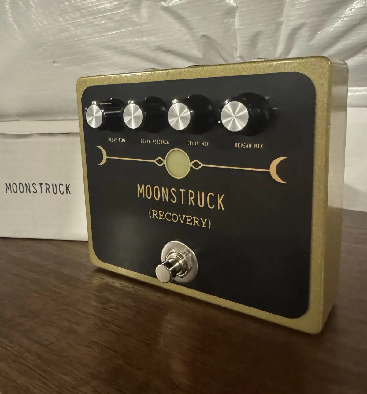 A black and gold guitar effects pedal labeled 'MOONSTRUCK (RECOVERY)' with four knobs for delay and reverb settings, a…